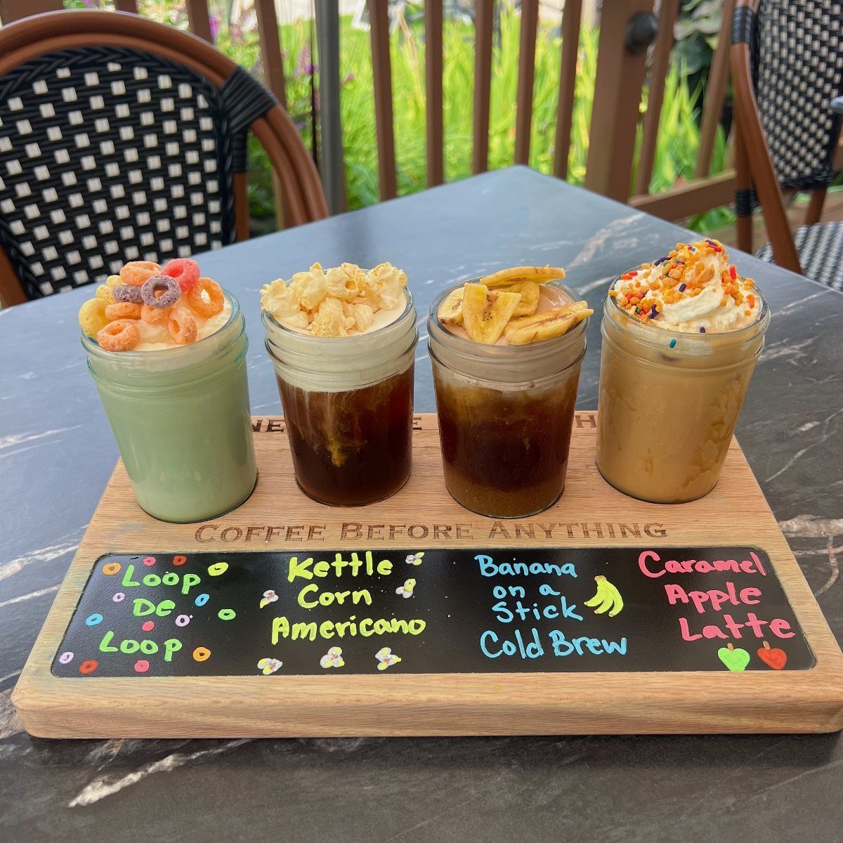 Four iced coffee drinks topped with carnival treats on a wooden serving tray.