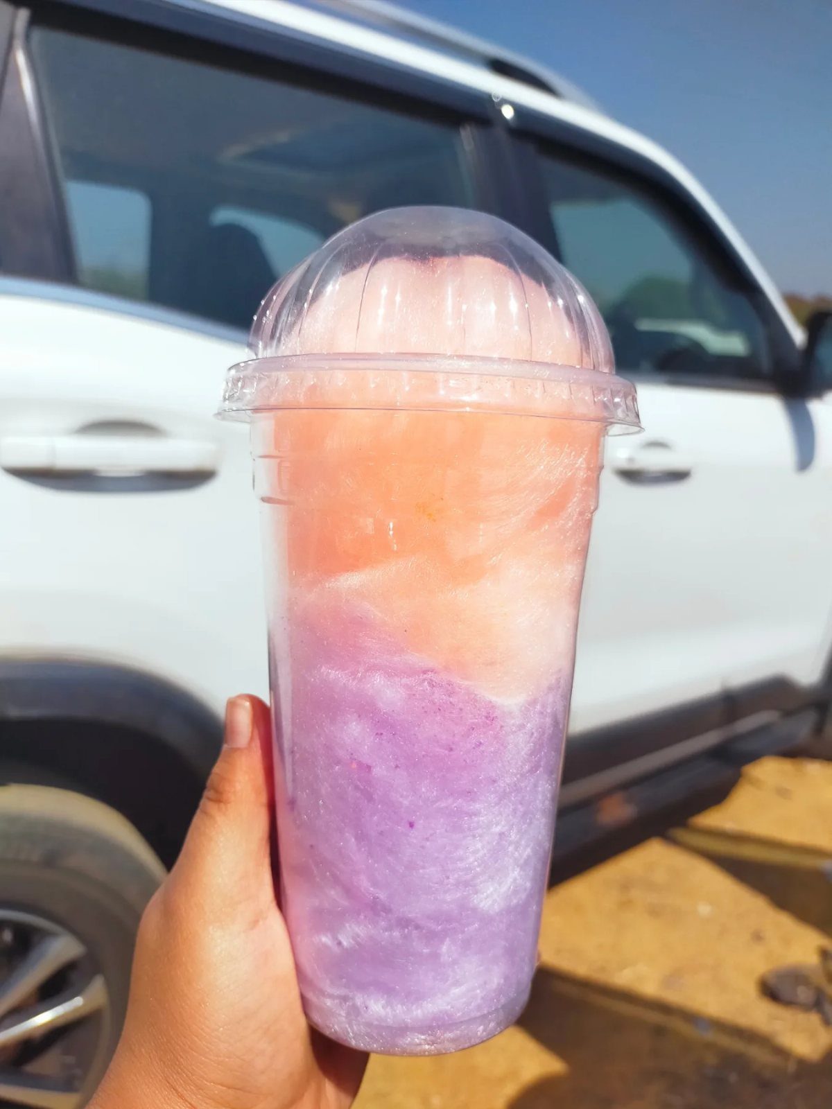 Cotton candy in pink, orange, and purple layers inside a plastic cup.