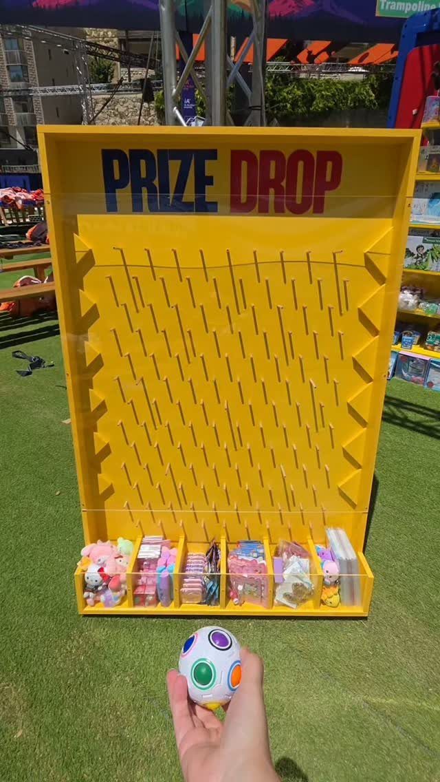 Yellow prize drop carnival game with toys at the bottom on green grass