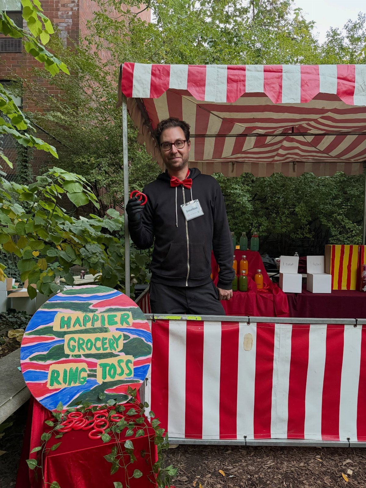 Man in bow tie standing behind a red and white striped ring toss booth.