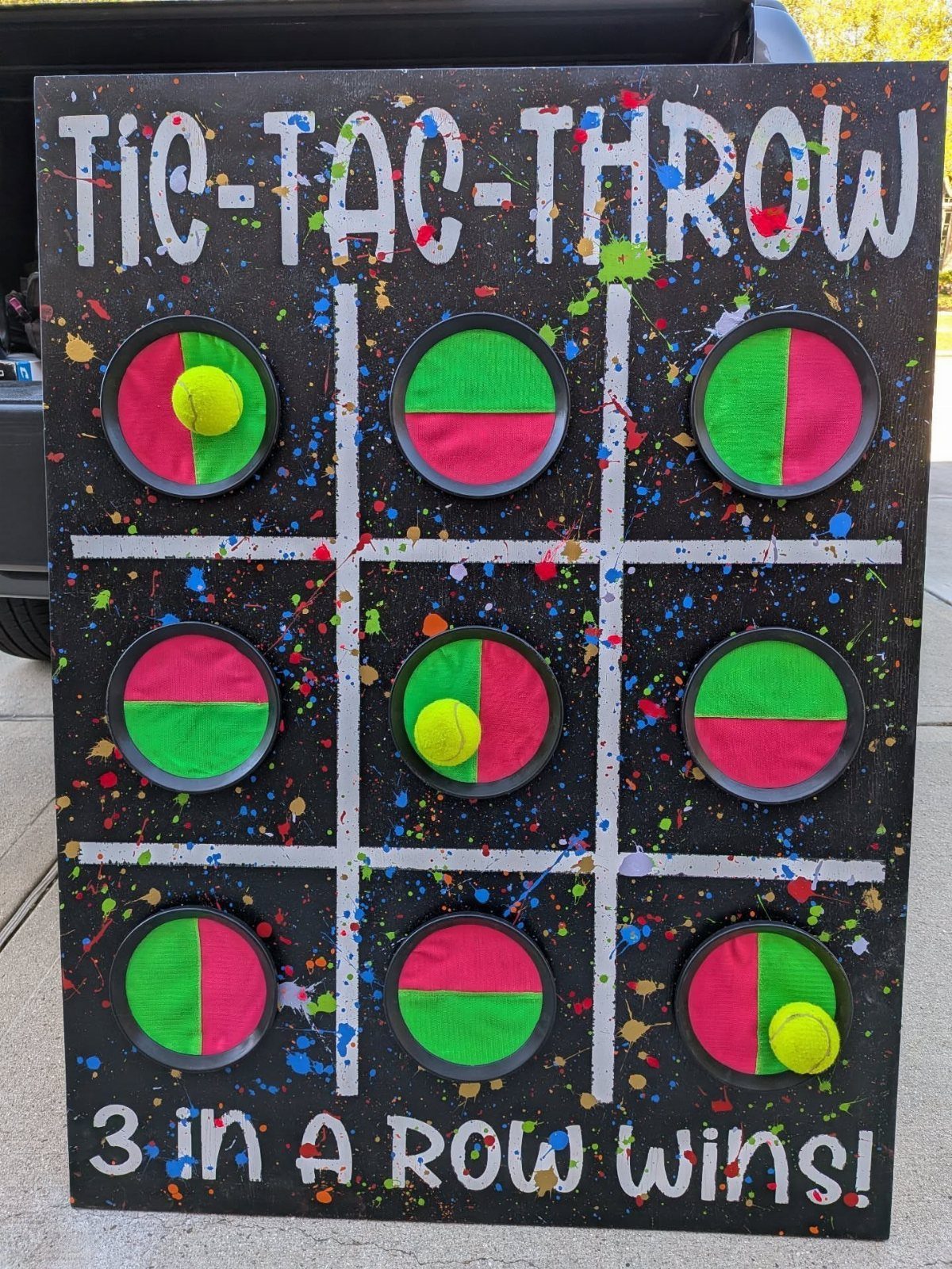 Tic-Tac-Throw carnival game board with colorful paint splatters and yellow balls