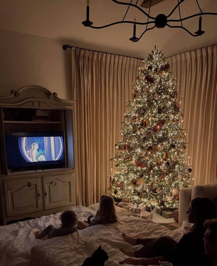 Family watching a movie on a bed next to a glowing Christmas tree