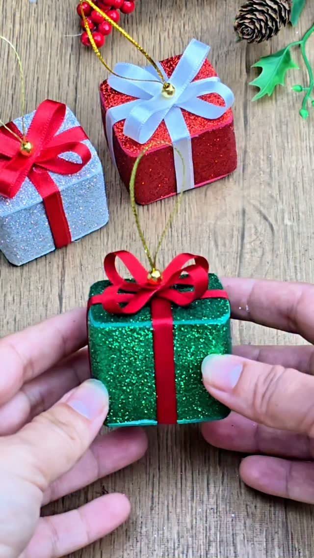 Hands holding a glittery green gift ornament on a wooden surface with decorations.