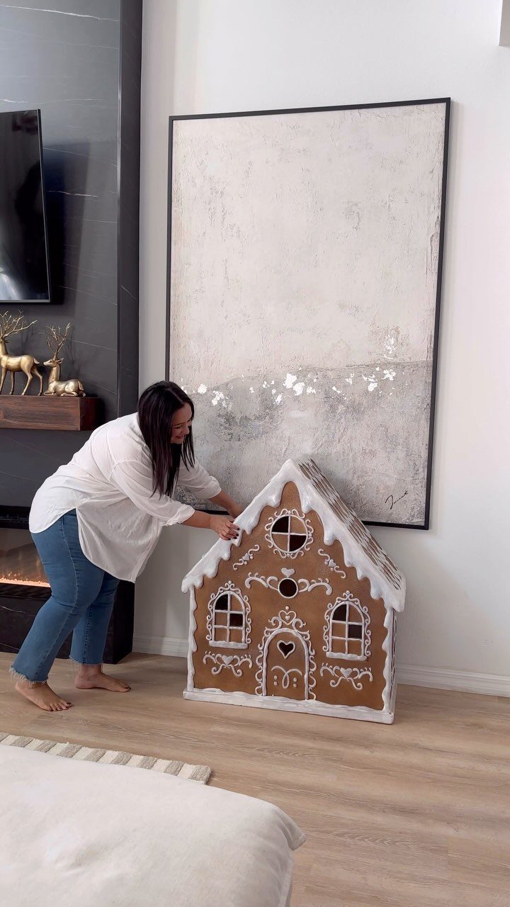 Woman setting up a large gingerbread house playhouse in a modern living room.