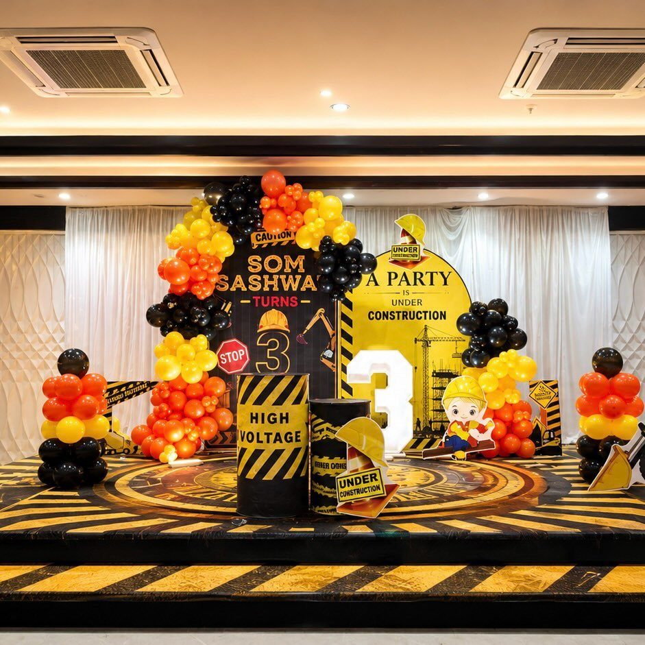 Construction-themed photo booth backdrop with yellow and black balloons and hazard stripes.