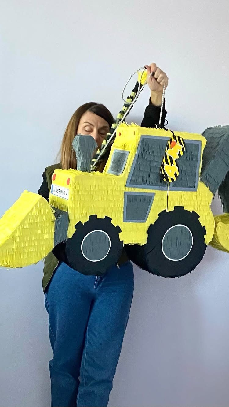 Yellow construction loader piñata held by a woman against a white wall.