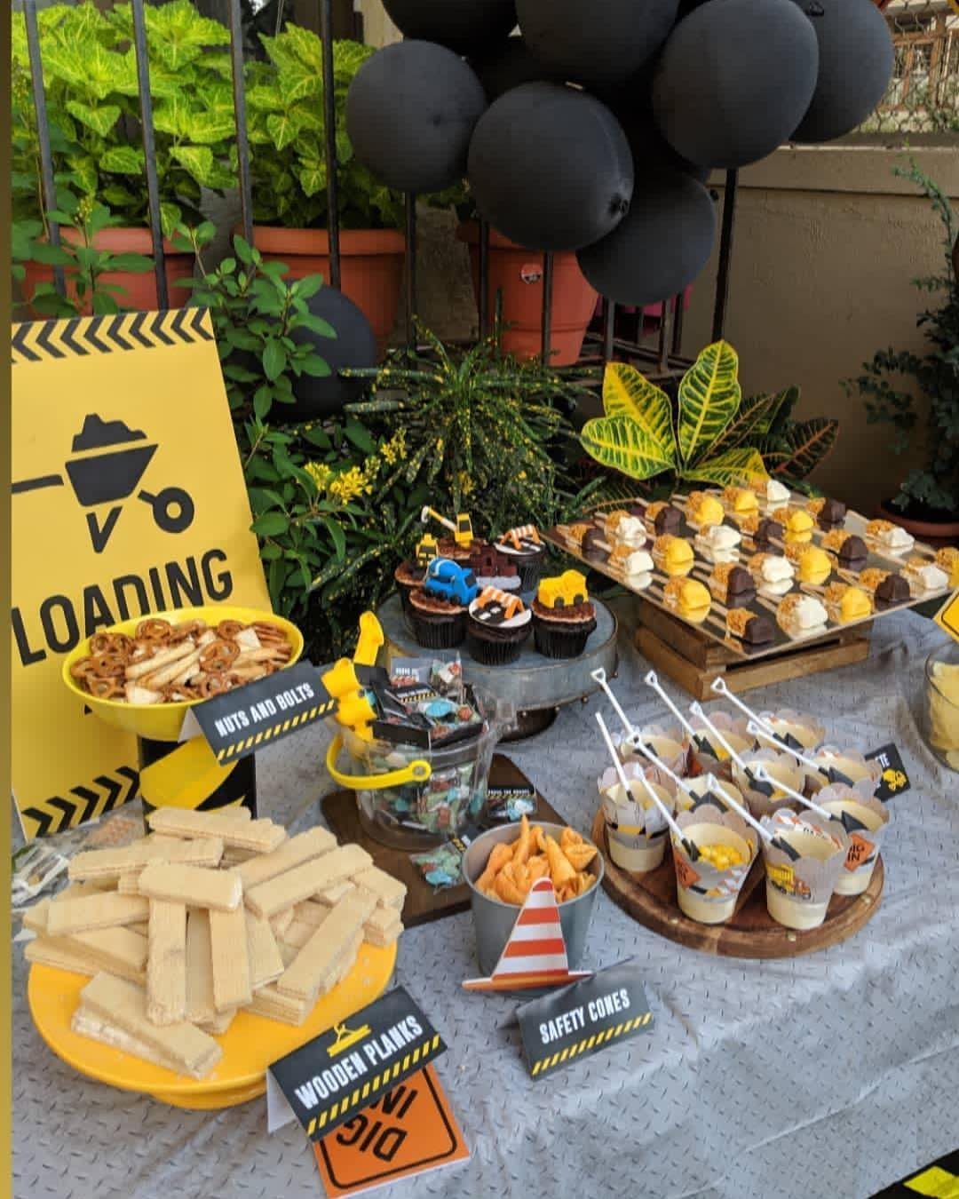 Construction-themed snacks on a table with yellow bowls, cupcakes, and themed signage.