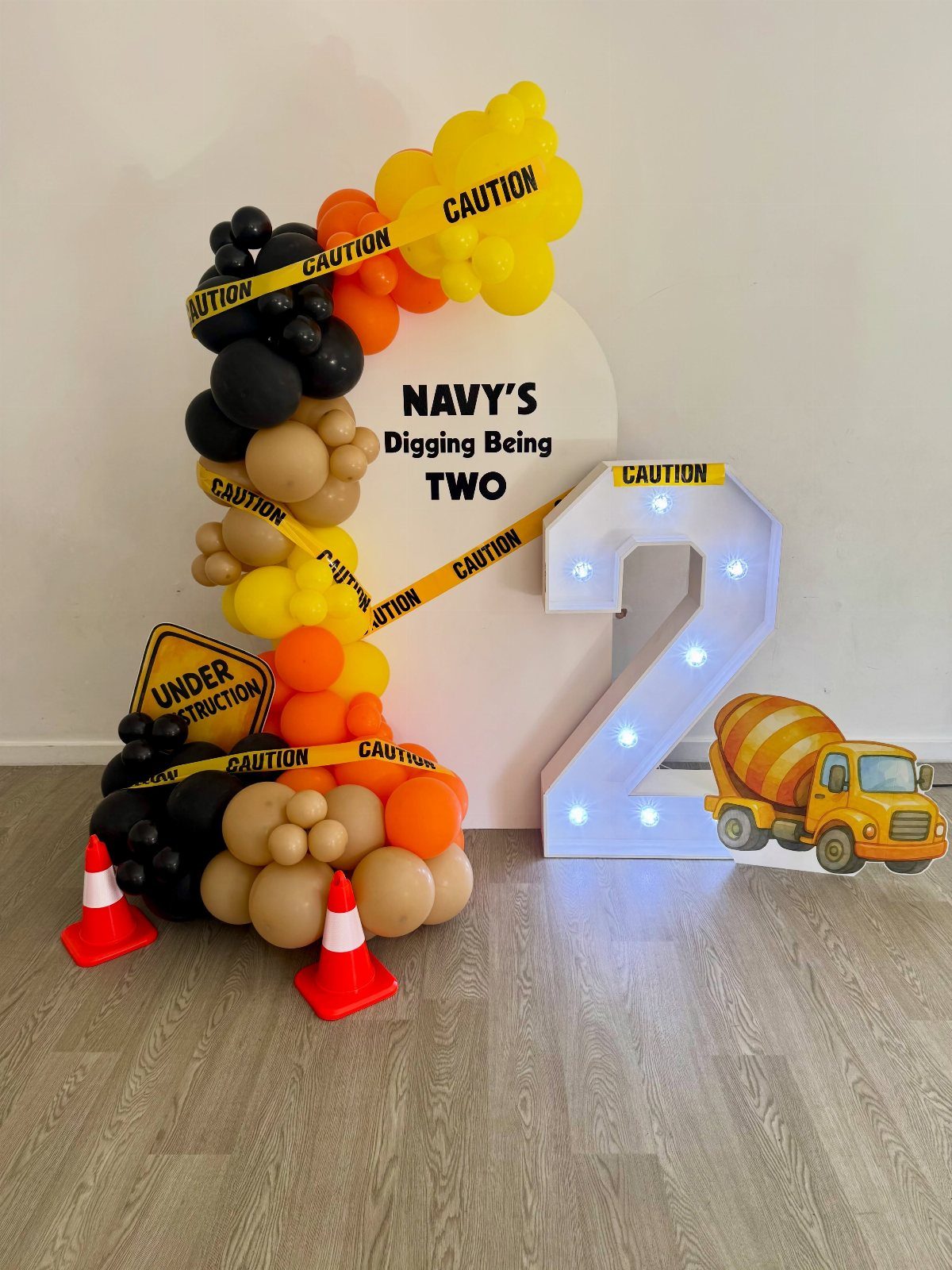 Construction party decor with yellow and black balloons, caution tape, and light-up number two.