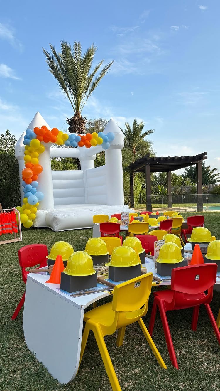 Outdoor construction party setup with yellow hard hats, traffic cones, and a bouncy castle.