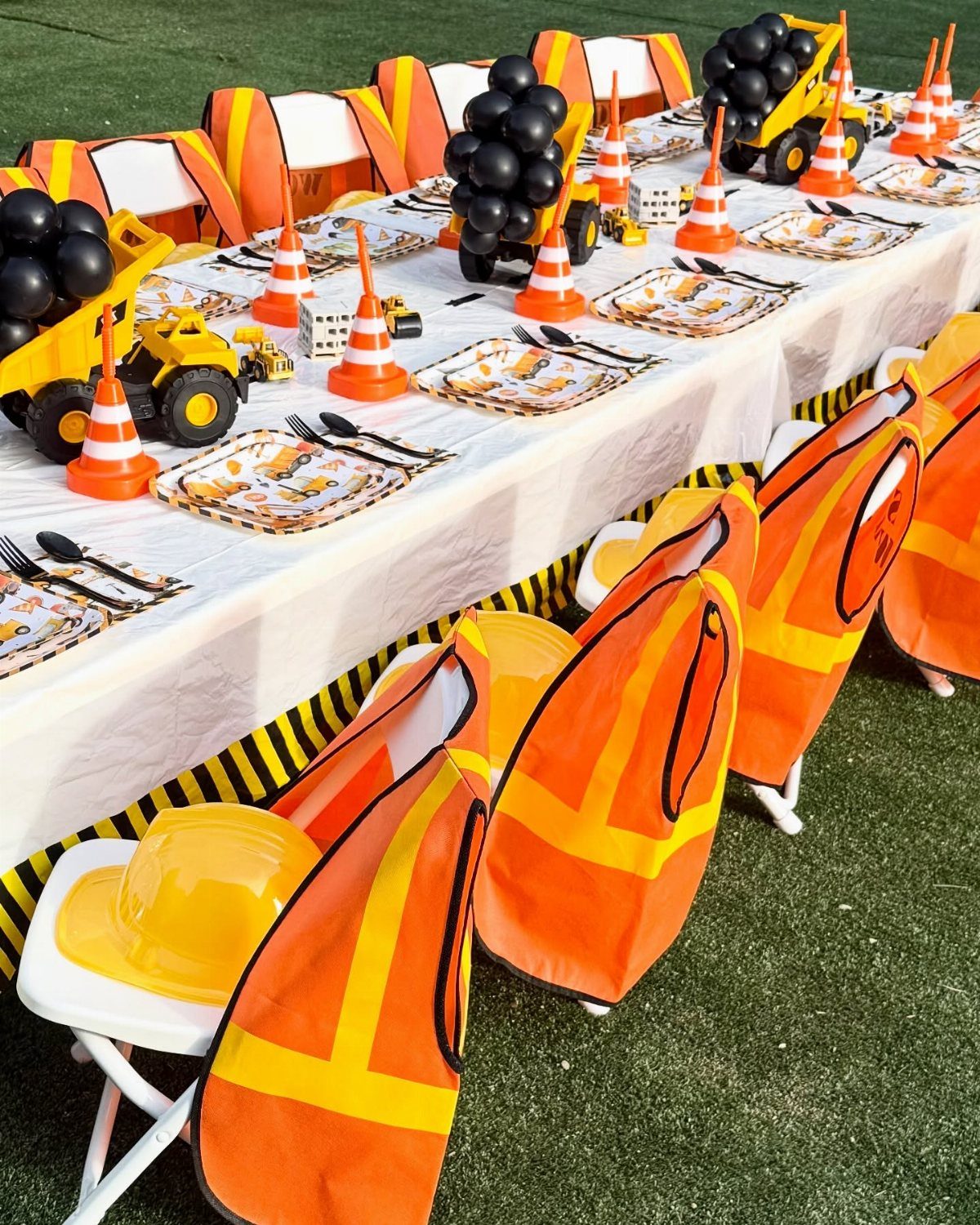 Construction party table setting with yellow and black plates, cones, and toy trucks.