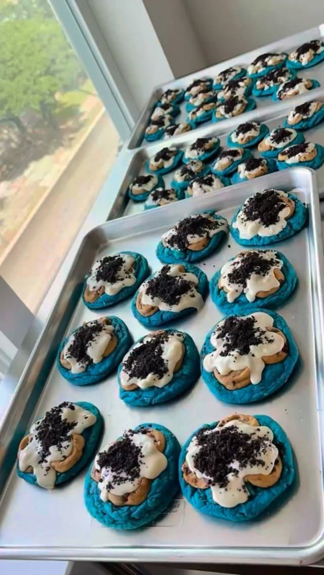 Blue cookies with white frosting and chocolate crumbs on metal baking sheets.