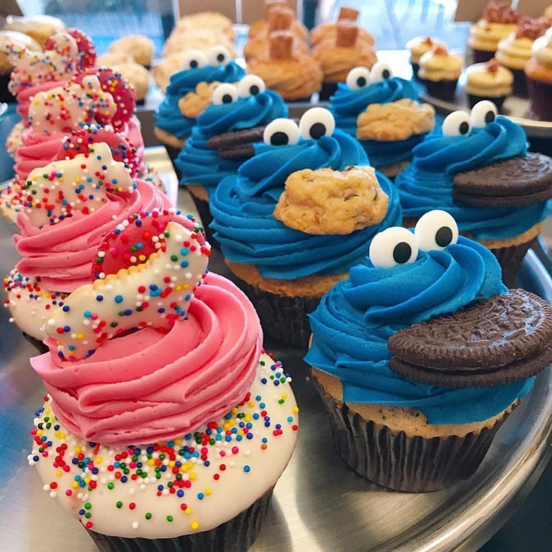 Cookie Monster themed cupcakes with blue frosting and cookies alongside pink sprinkled cupcakes.