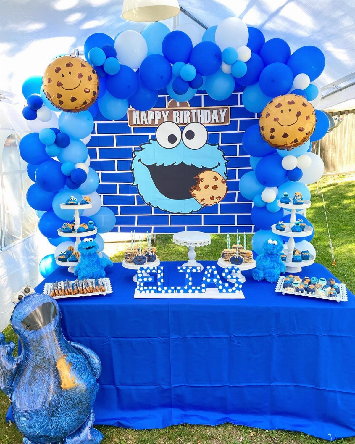 Cookie Monster themed dessert table with blue balloons, treats, and a character backdrop.