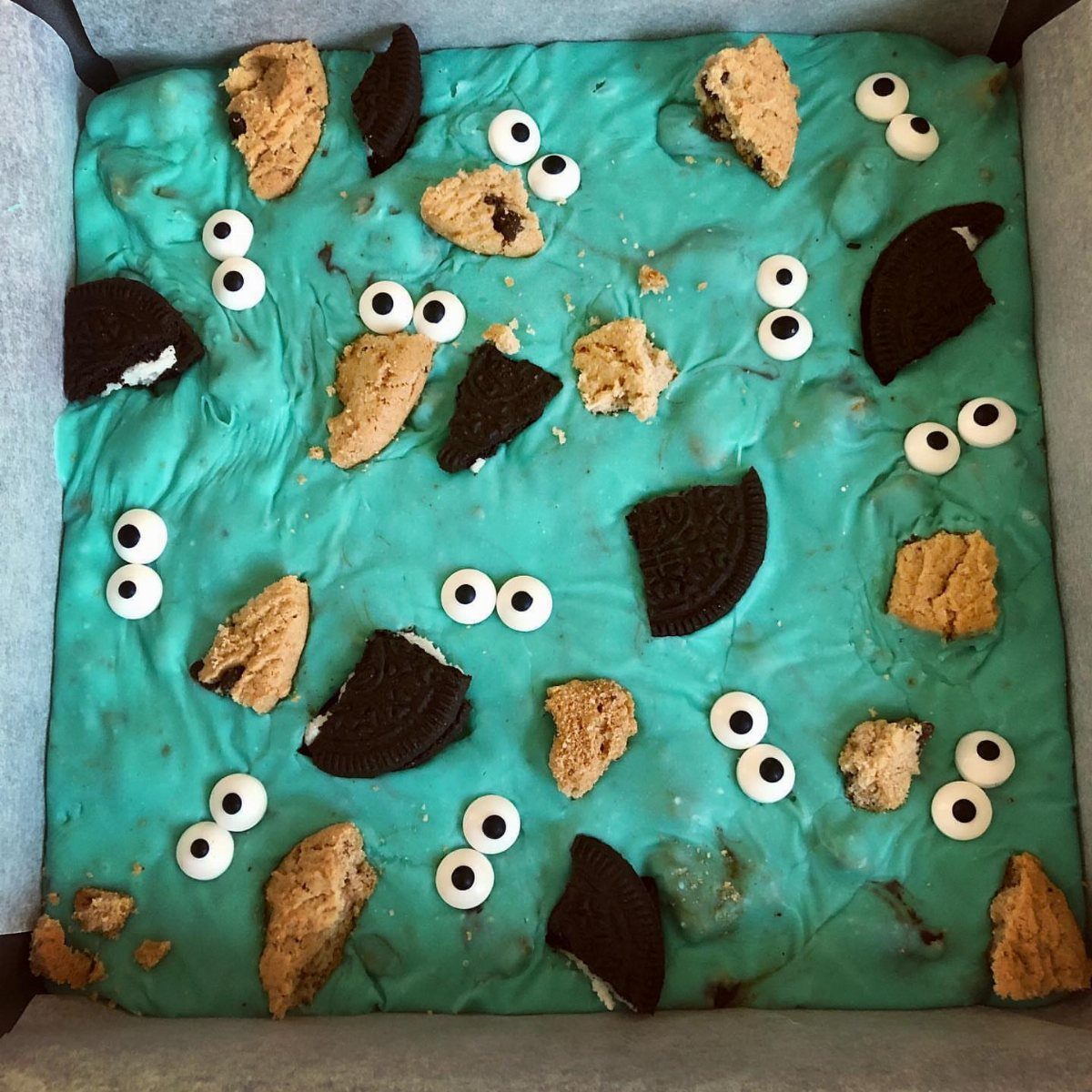Blue fudge topped with broken cookies and candy eyes in a square pan.