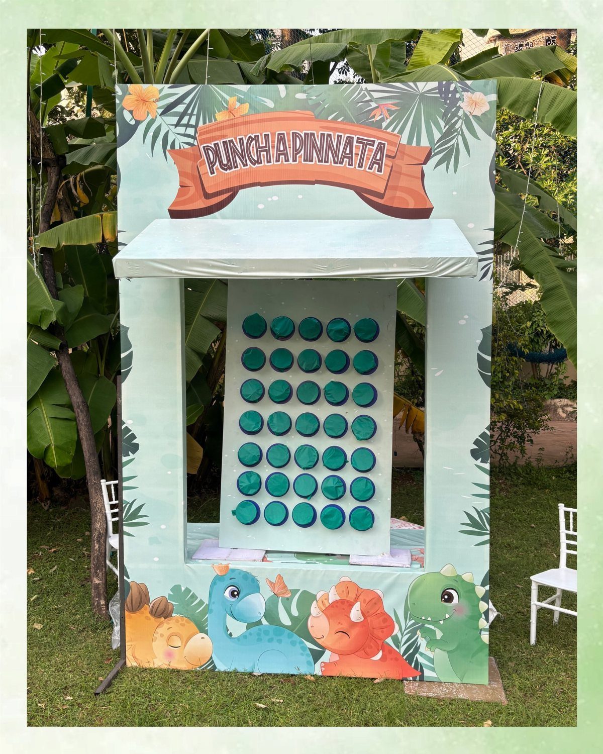 Dinosaur themed punch-a-piñata game booth with cartoon dinosaurs on a green lawn.