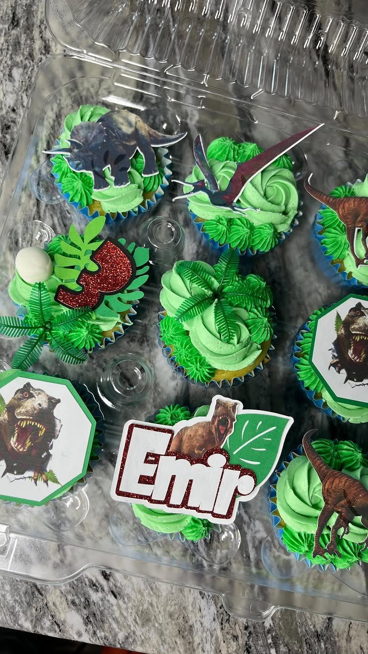 Dinosaur themed cupcakes with green frosting and dinosaur toppers in a plastic container.