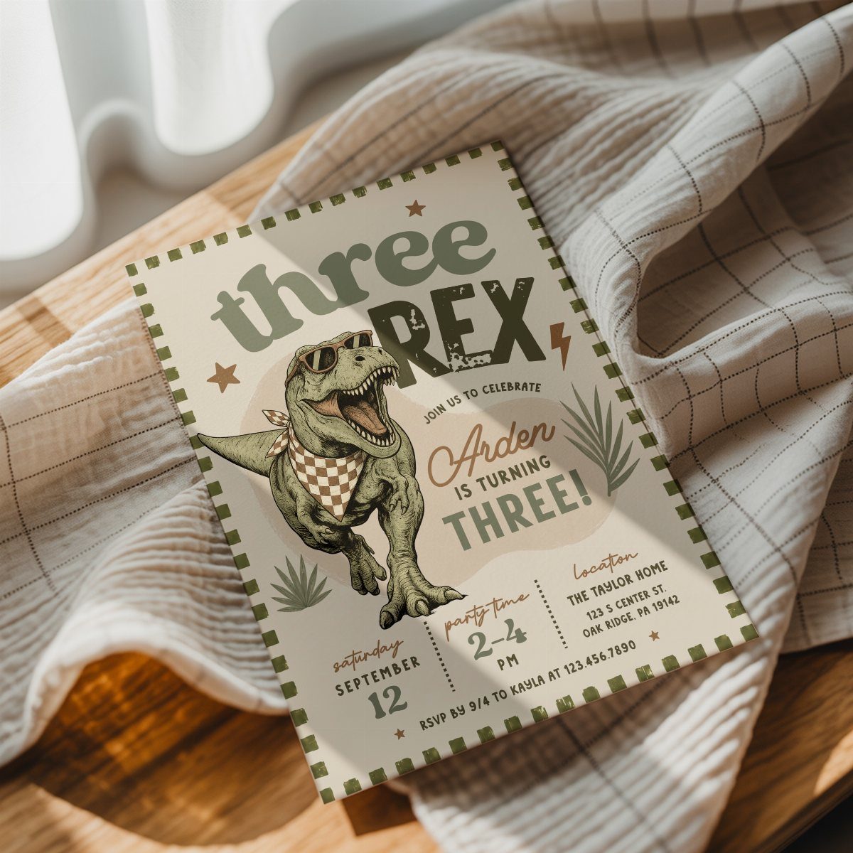 Dinosaur themed birthday invitation with a T-Rex on a wooden table and cloth