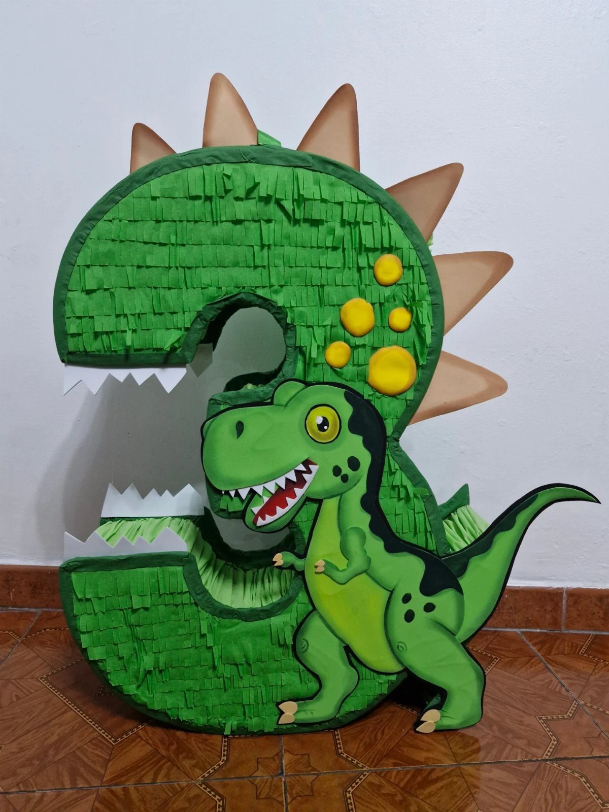 Number three shaped green dinosaur piñata with spikes and a cartoon dinosaur figure.