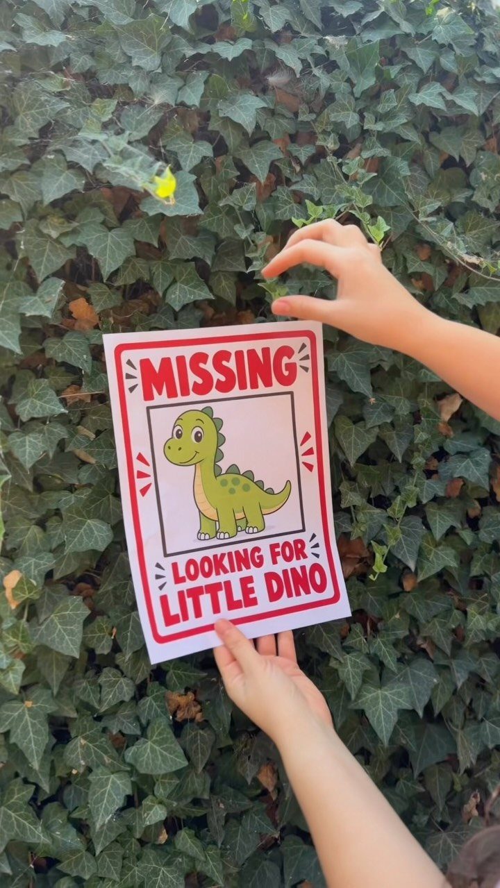 Hands holding a missing dinosaur sign against a lush green ivy wall.