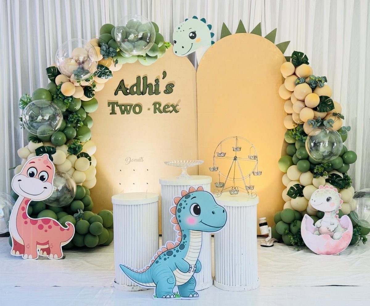 Dinosaur party backdrop with yellow arches, balloon garlands, and cute dinosaur cutouts.