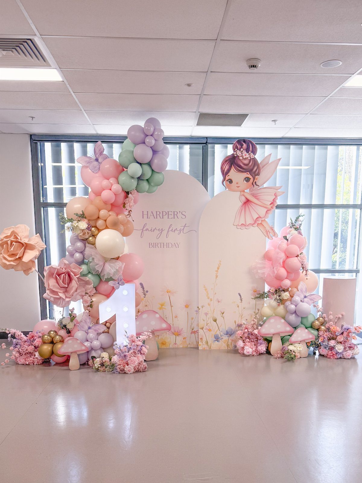 Fairy themed photo backdrop with pastel balloons, mushrooms, and a fairy cutout.