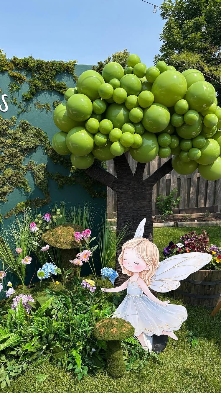 Outdoor fairy party setup with a green balloon tree and fairy cutout.