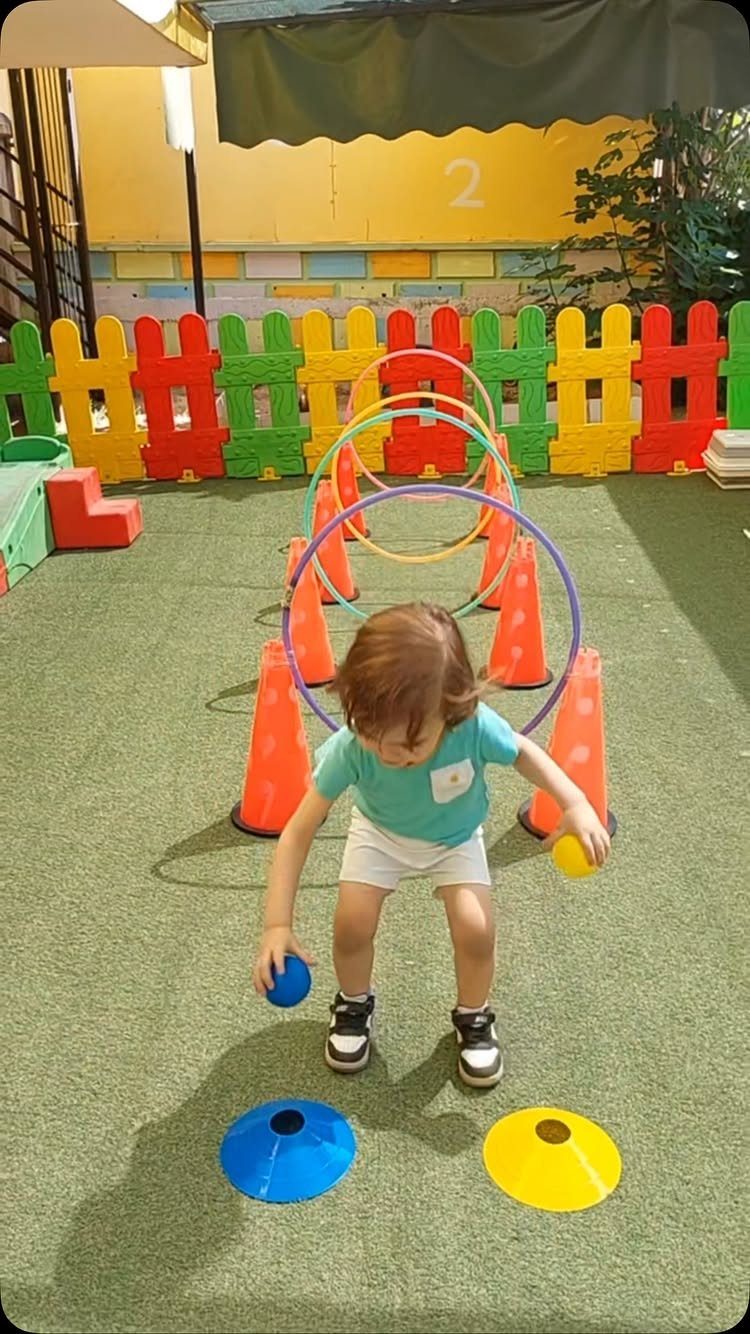 Toddler playing in an obstacle course with colorful hula hoops and orange cones.