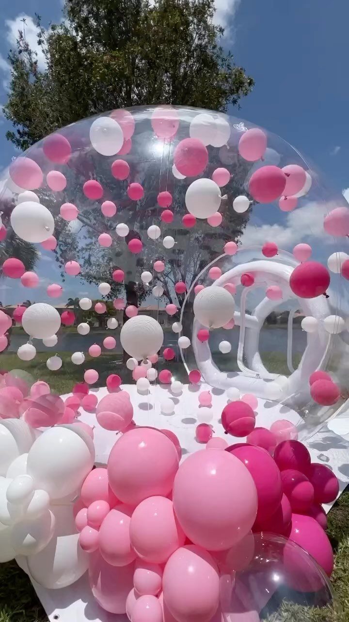 Clear inflatable dome filled with pink and white balloons on a grassy lawn