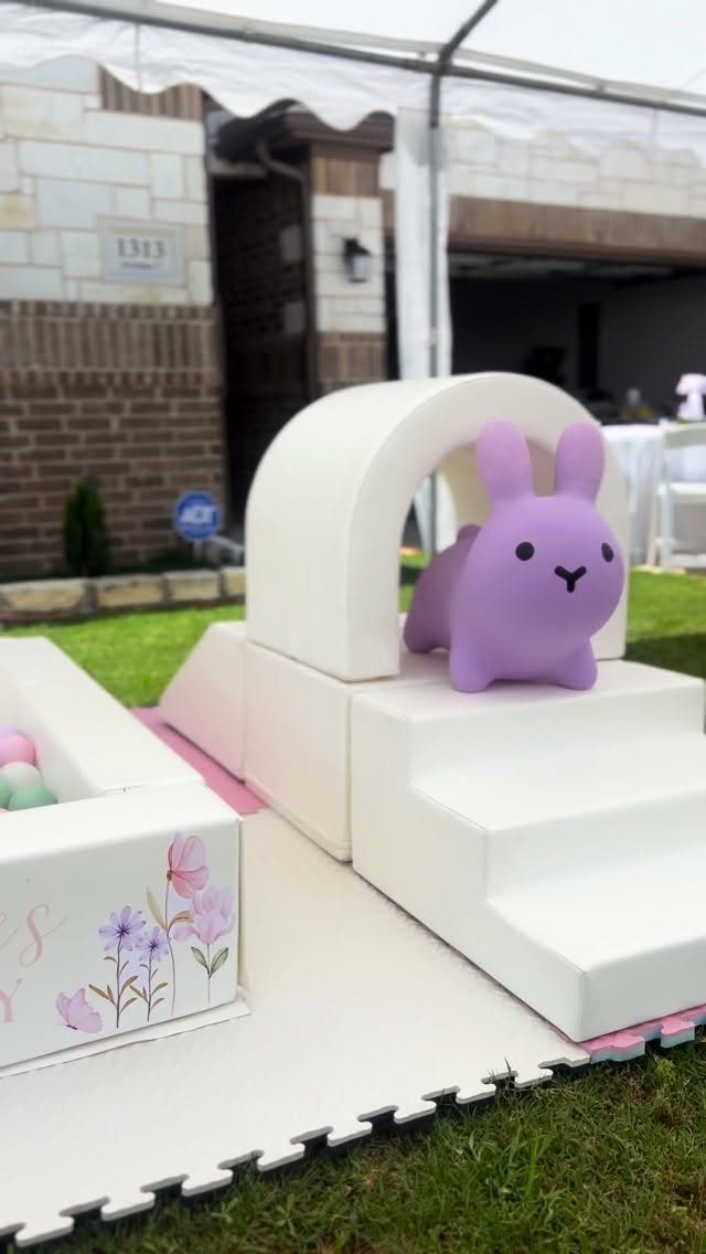 Purple rabbit toy on white foam blocks and steps on a grassy lawn