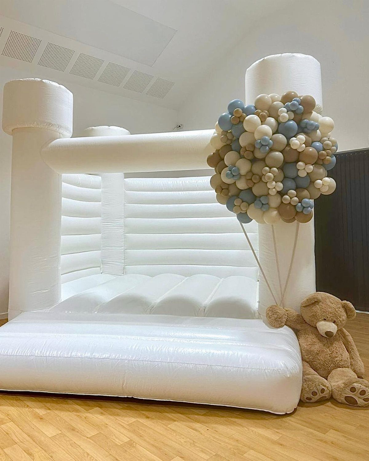 White inflatable bouncy castle with blue and tan balloons and a teddy bear.