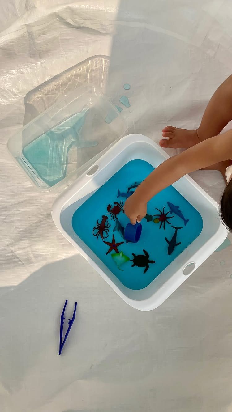 Child playing with plastic sea animals in a blue water sensory bin.