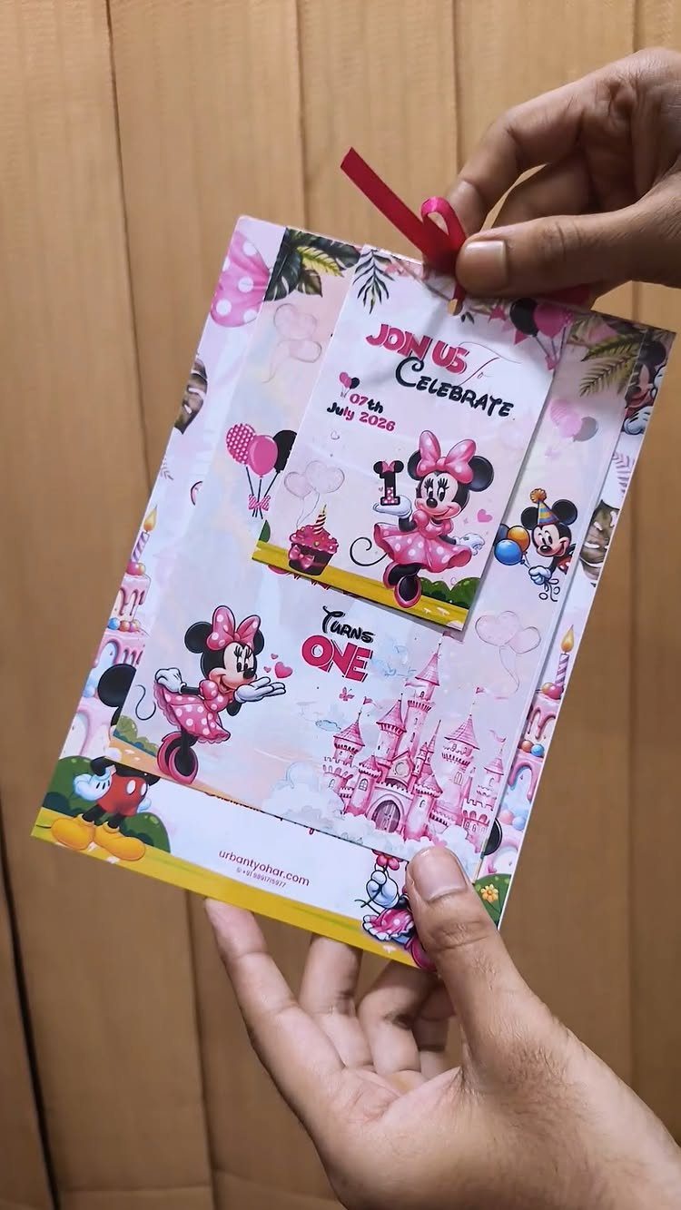 Minnie Mouse themed first birthday invitation card held by two hands.
