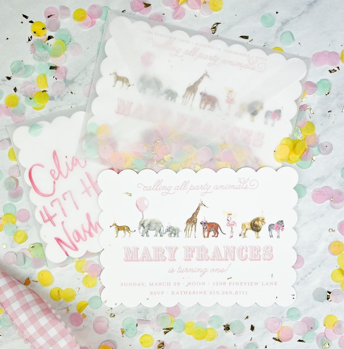 First birthday invitation with watercolor animals and a translucent envelope on marble.