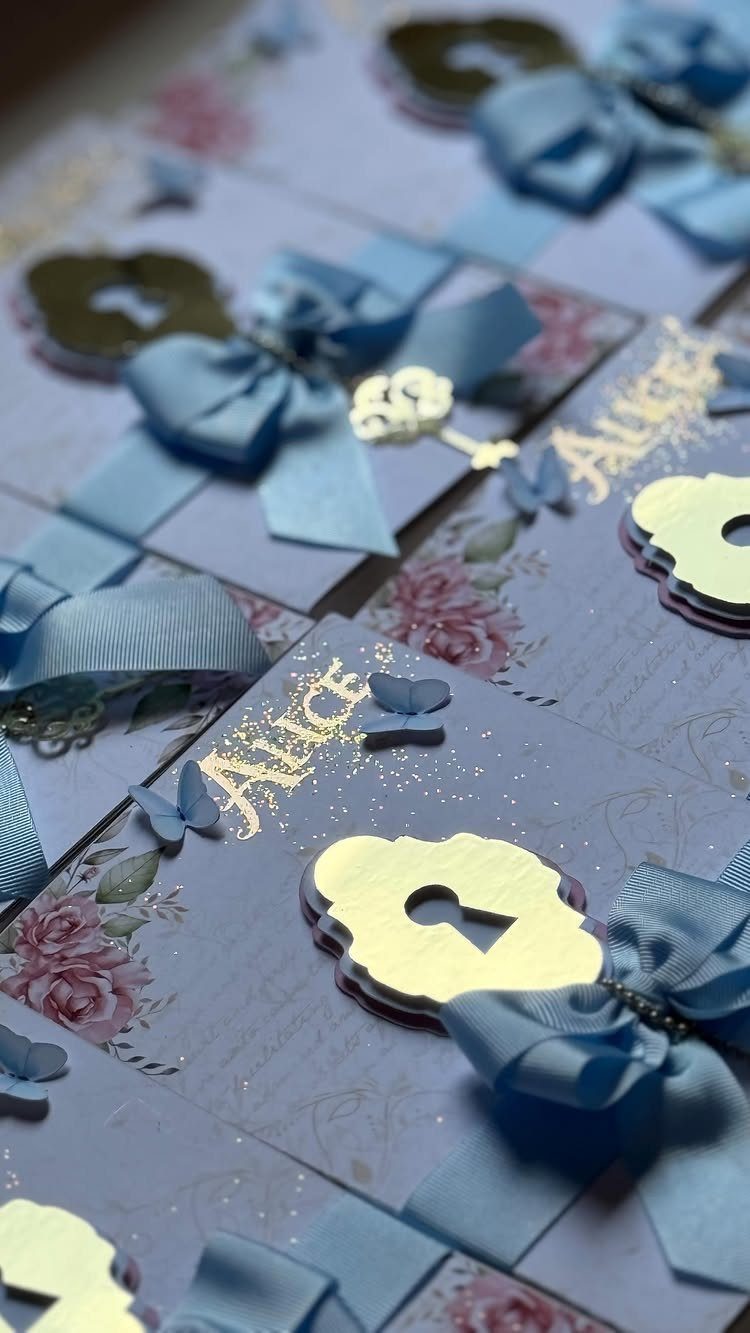 Purple floral invitations with blue satin bows and gold key charms for Alice.