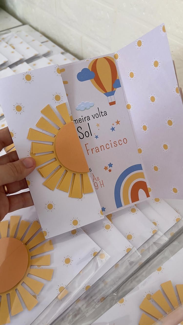 Open birthday invitation with a yellow sun cutout, hot air balloon, and rainbow.