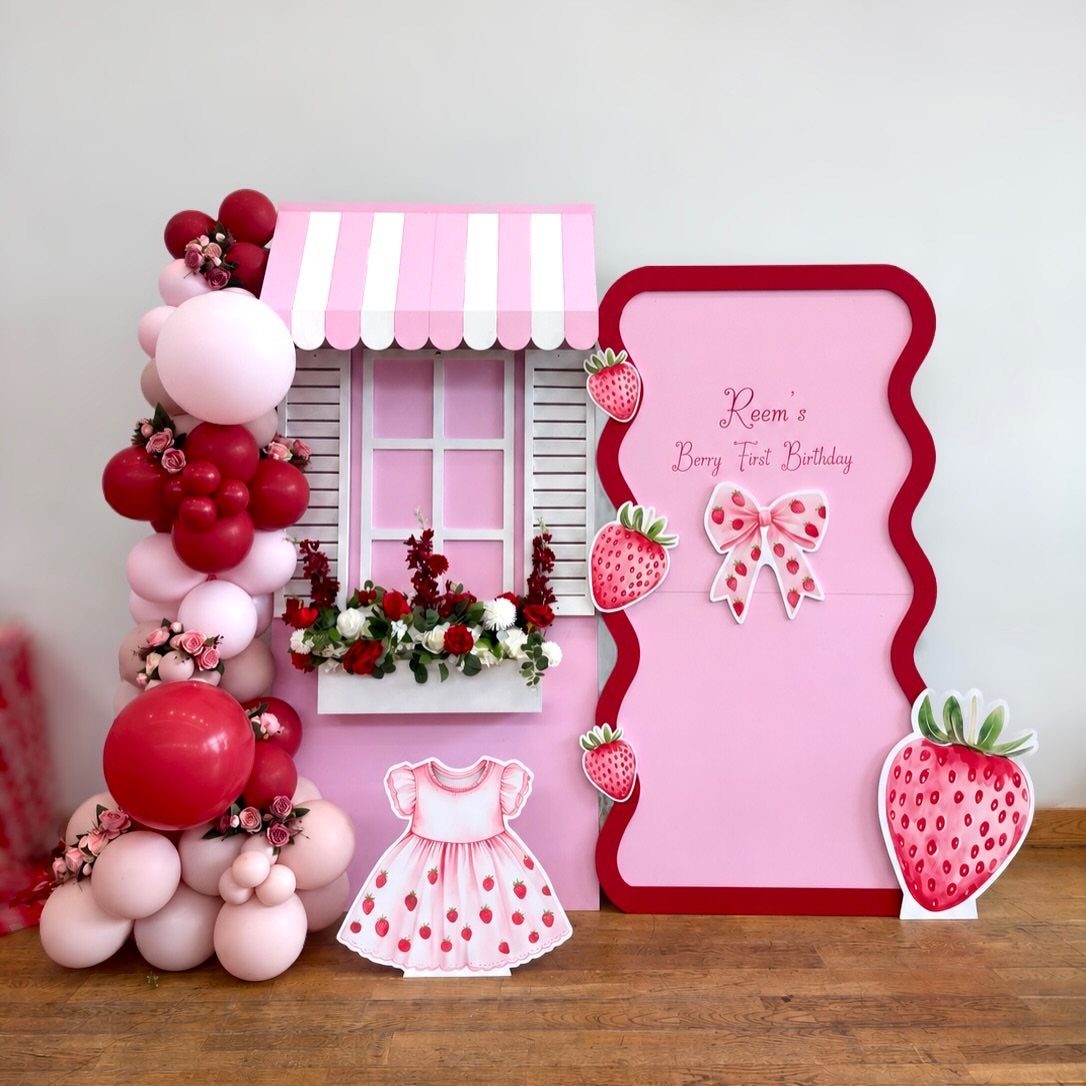 Pink birthday party setup with strawberry decorations, red balloons, and a miniature storefront.