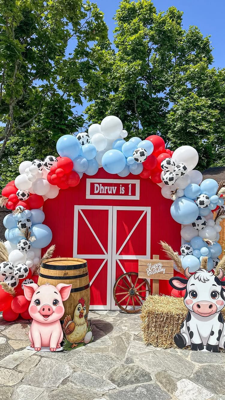 Red barn backdrop with farm animal cutouts and balloons for a first birthday.