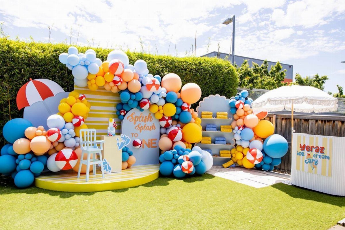 Beach themed first birthday party setup with colorful balloons and beach umbrellas.