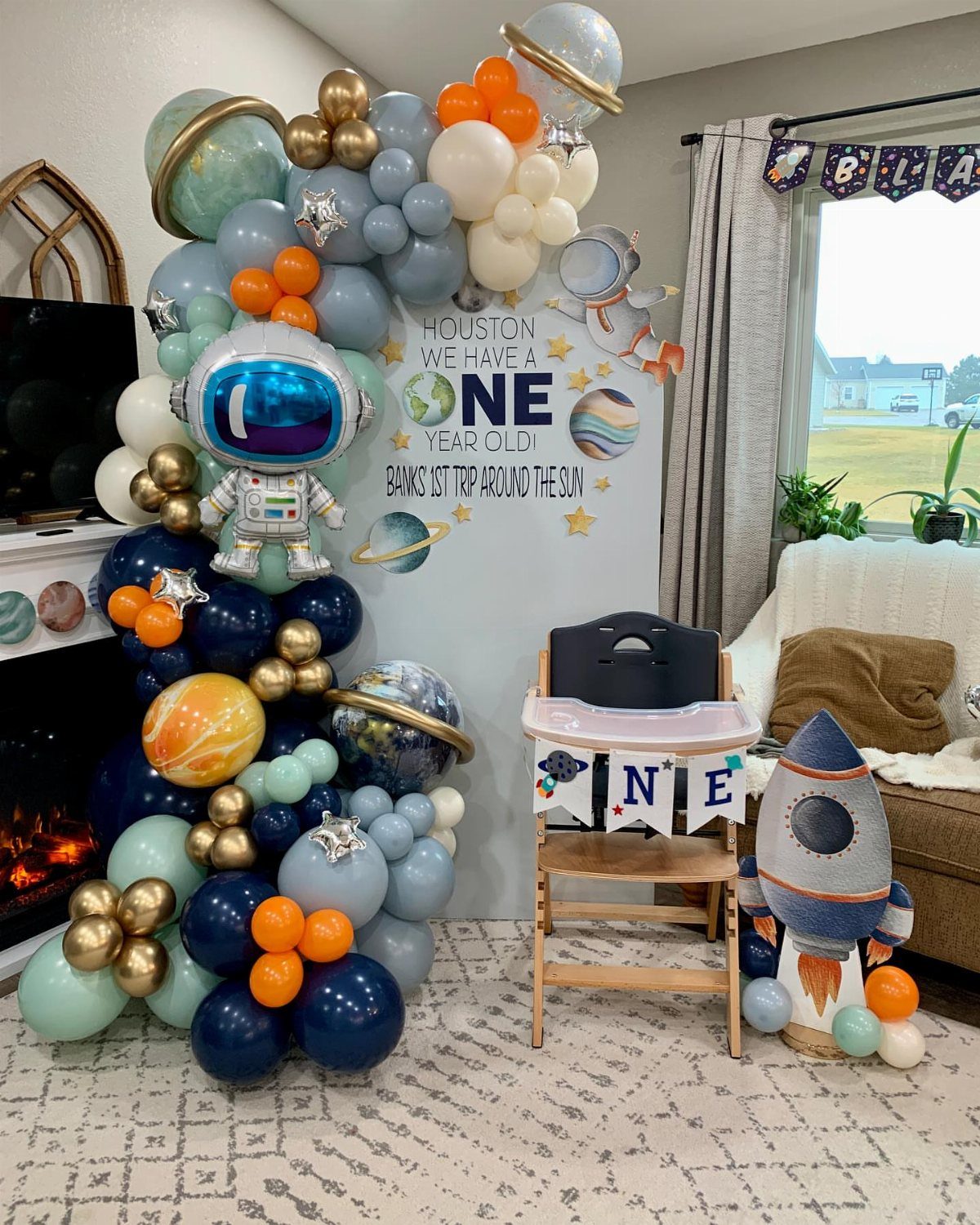 Space-themed first birthday party setup with balloon arch, astronaut, and rocket ship prop.
