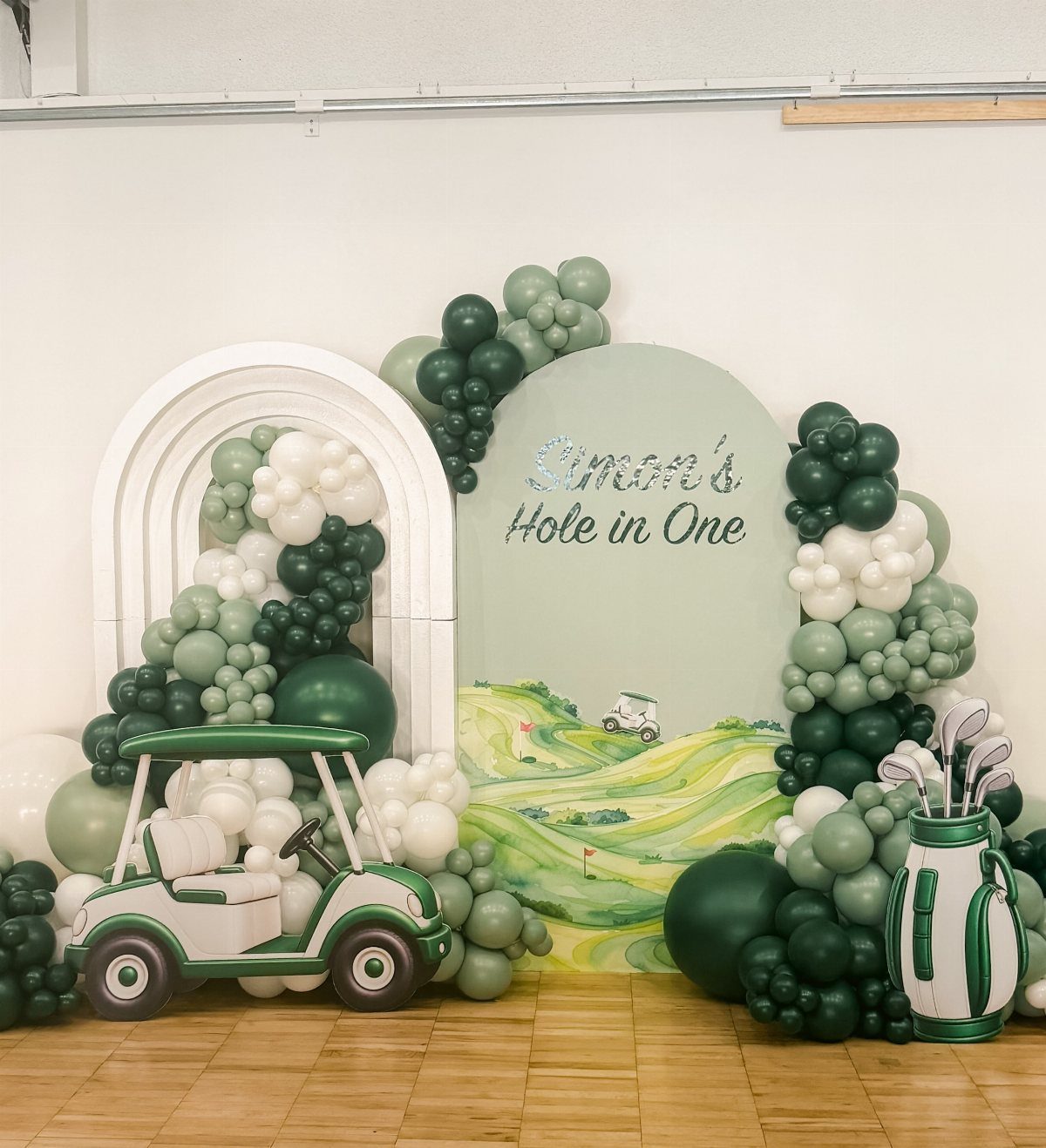 Golf themed birthday backdrop with green balloons, a golf cart, and Hole in One text.
