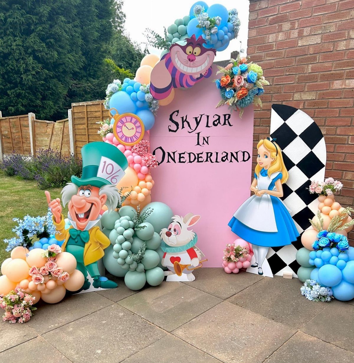 Alice in Wonderland party setup with character cutouts, balloons, and a pink backdrop.