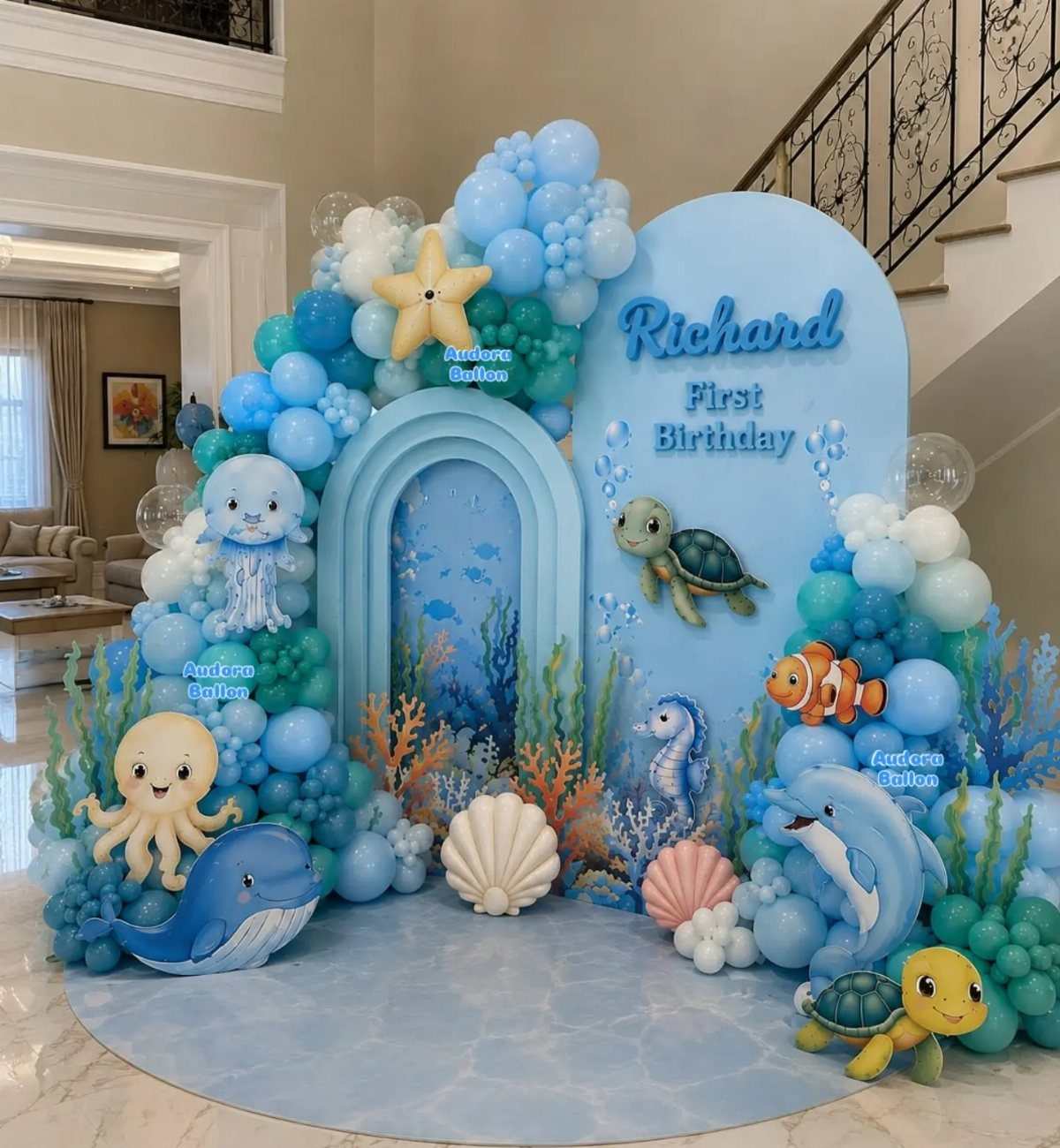 Ocean-themed first birthday party backdrop with blue balloons and cartoon sea creatures.