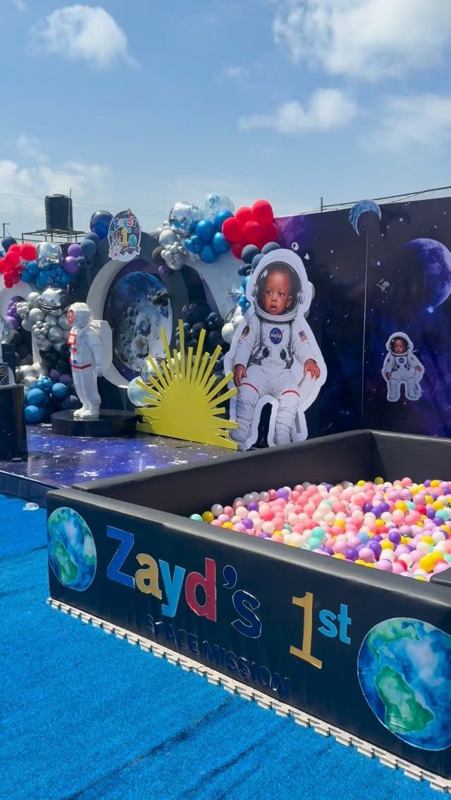 Space themed first birthday party setup with astronaut cutout and colorful ball pit.