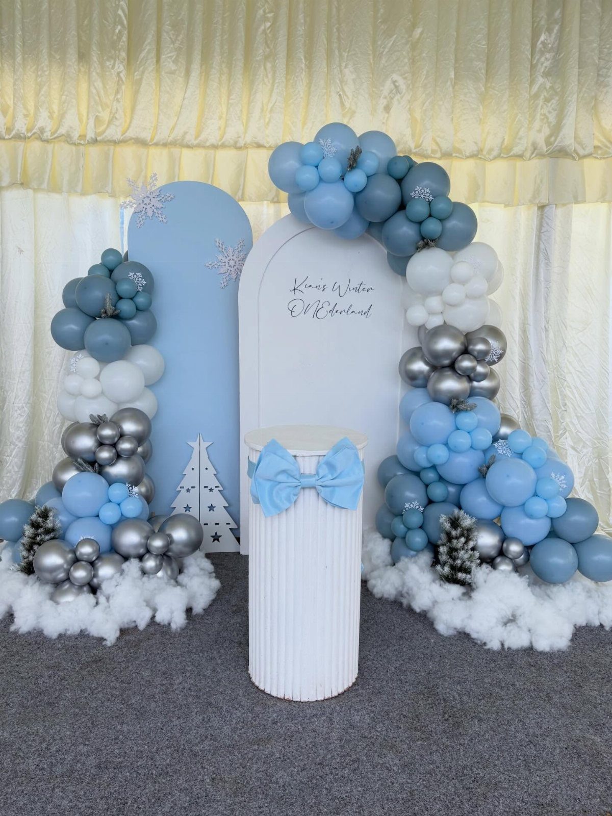 Blue and silver balloon garlands with snowflakes and white fluffy clouds backdrop.