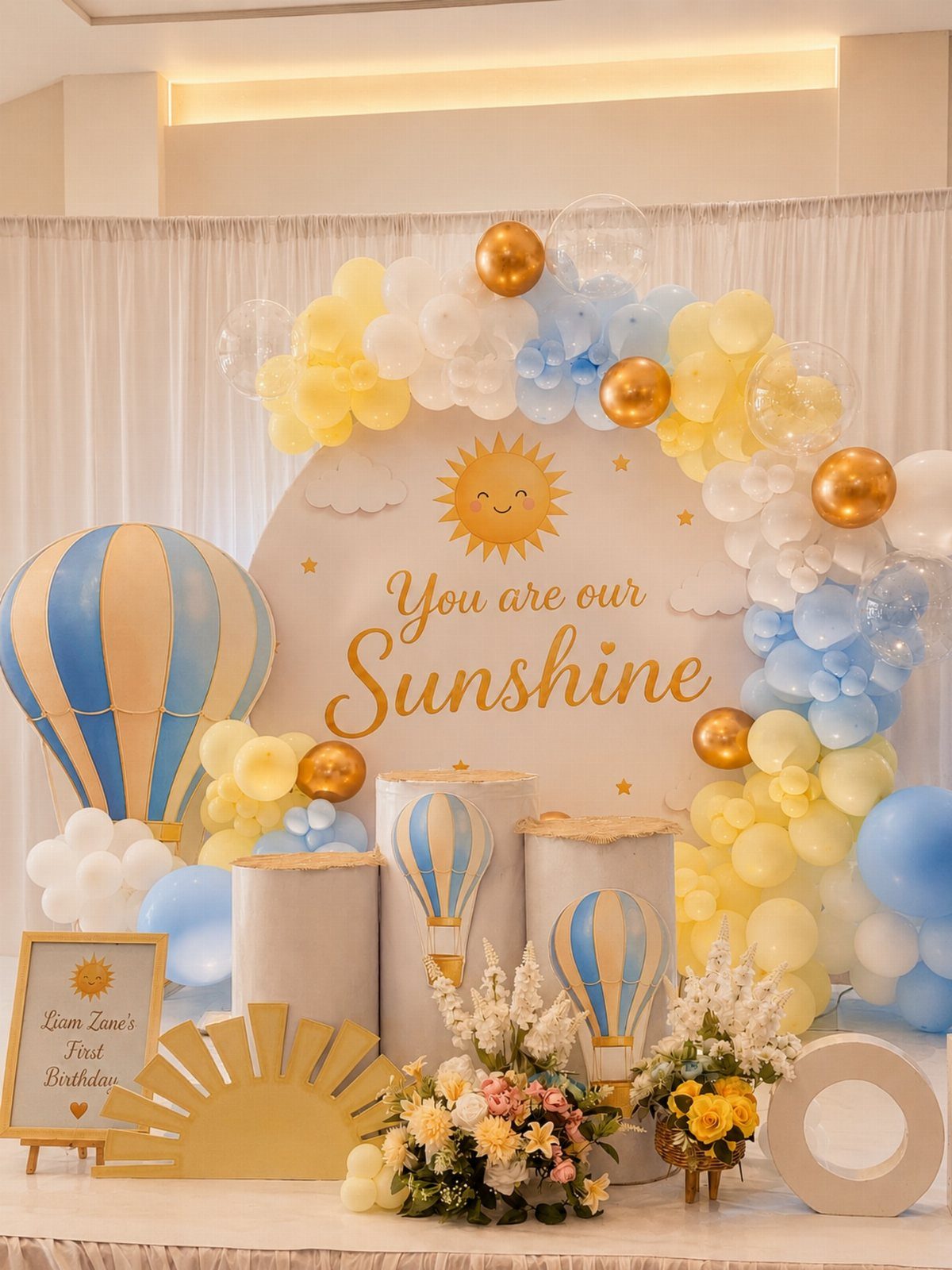 Sunshine themed birthday party decoration with yellow balloons and a smiling sun backdrop.