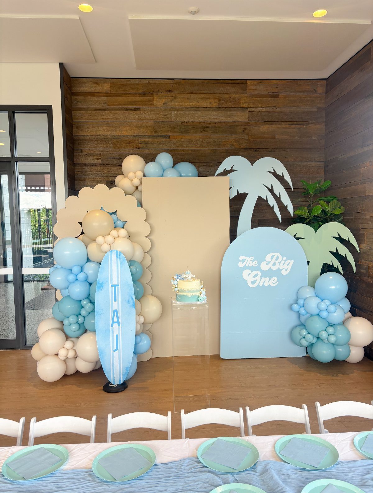 Surfboard and palm tree decorations with blue and beige balloons for a birthday.