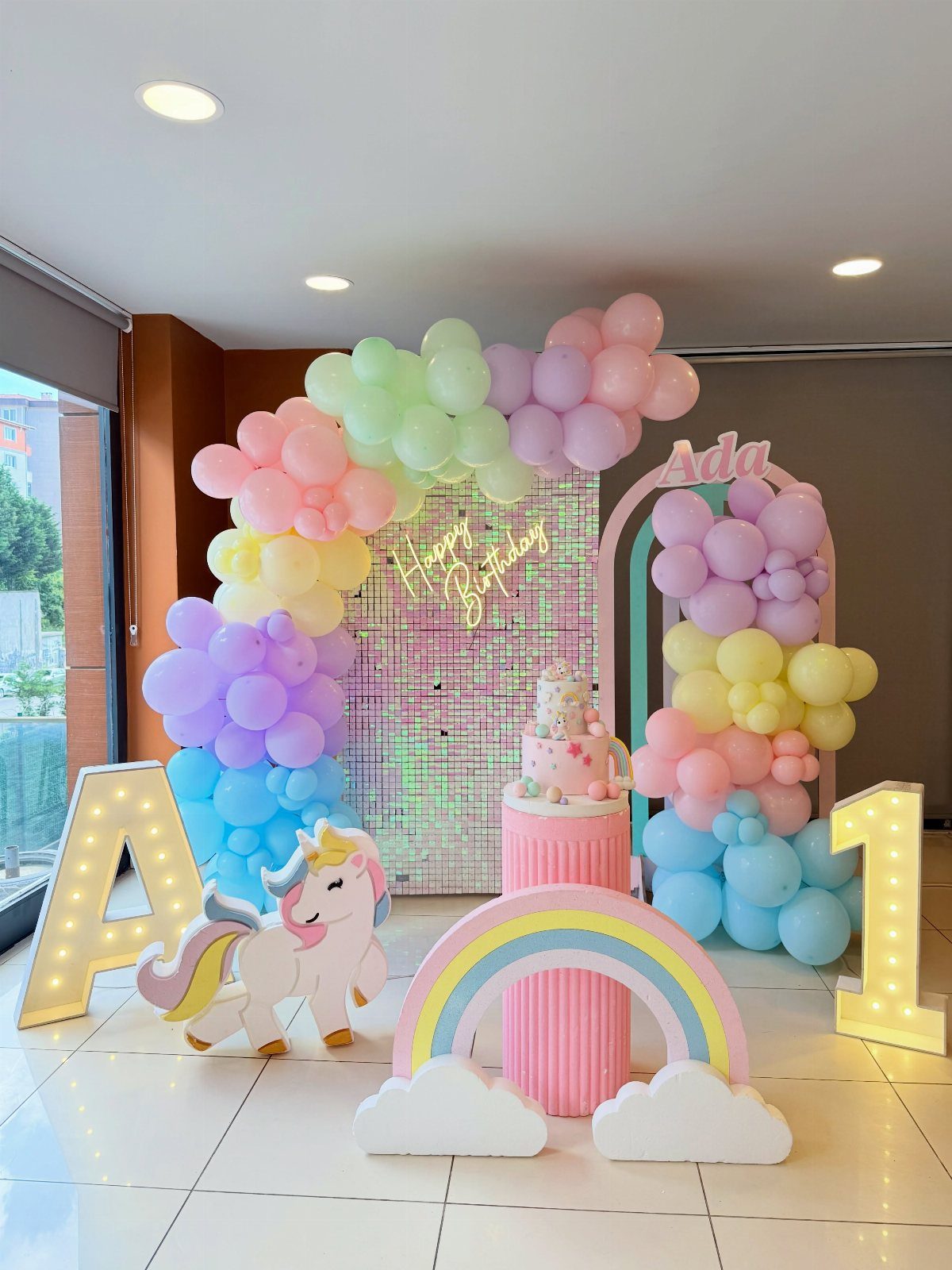 Pastel rainbow balloon arch and unicorn cutout for a first birthday party setup.