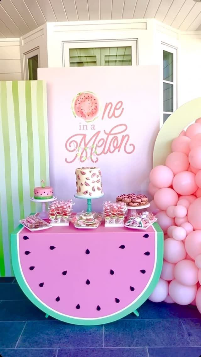 Watermelon shaped dessert table with themed cakes and pink balloon decorations.