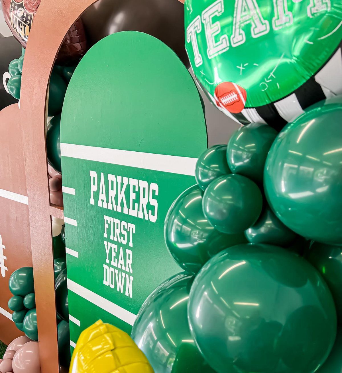 Football themed birthday party backdrop with green balloons and yard line signage.