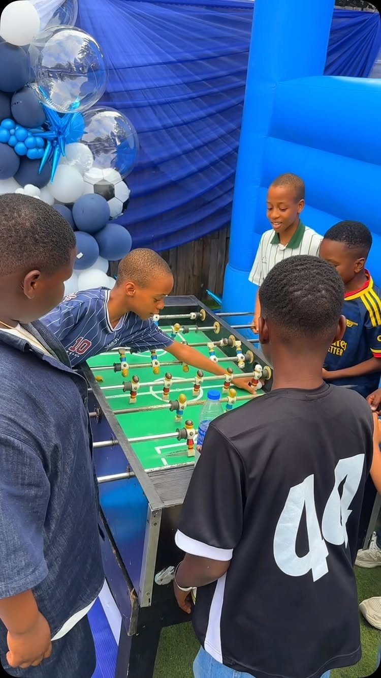 Boys playing foosball at a party with blue and white balloon decorations.